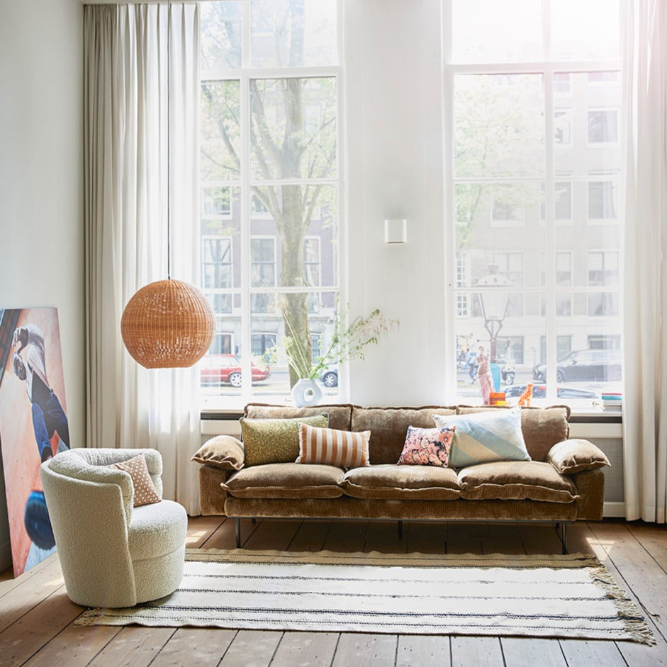 big brown round hanging light made of weaved bamboo in a living room with a sofa and a chair and art work