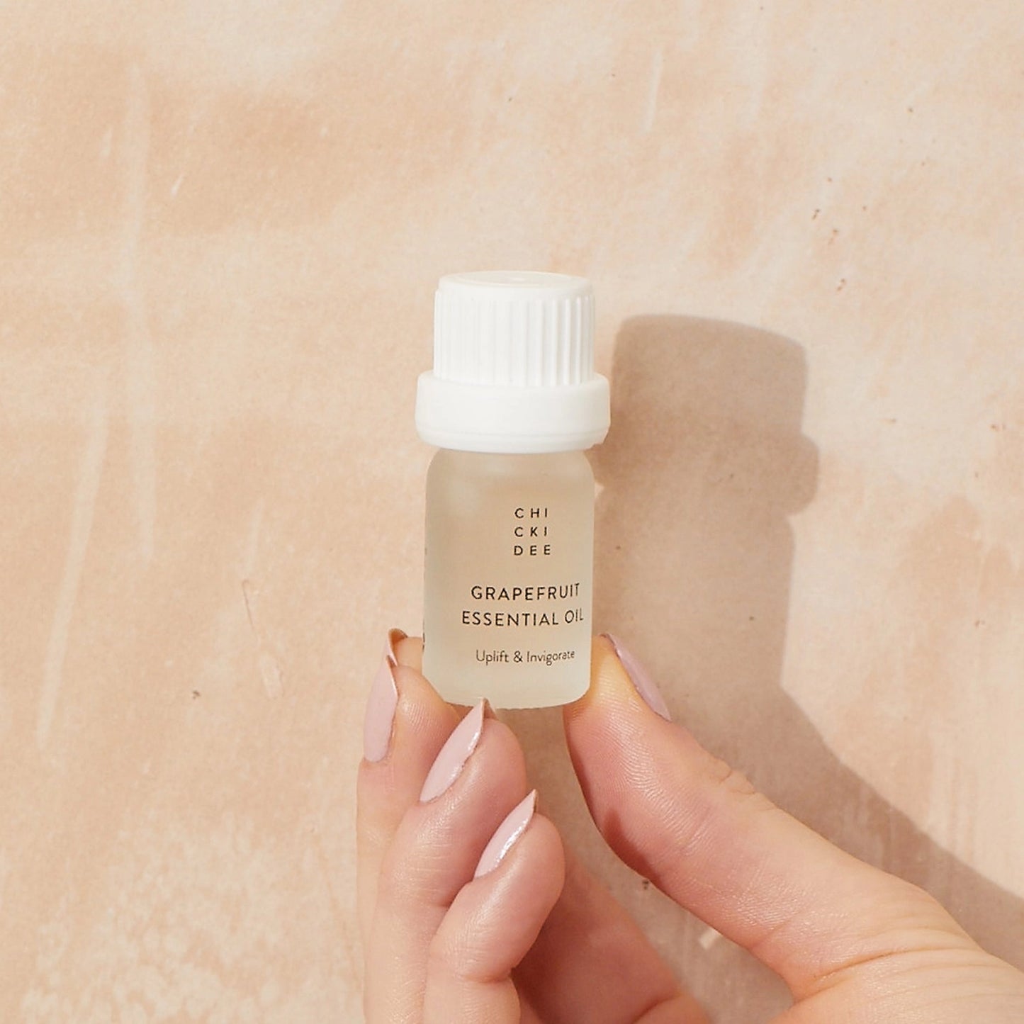 hand holding a 5ml small glass jar with cap filled with grapefruit essential oil
