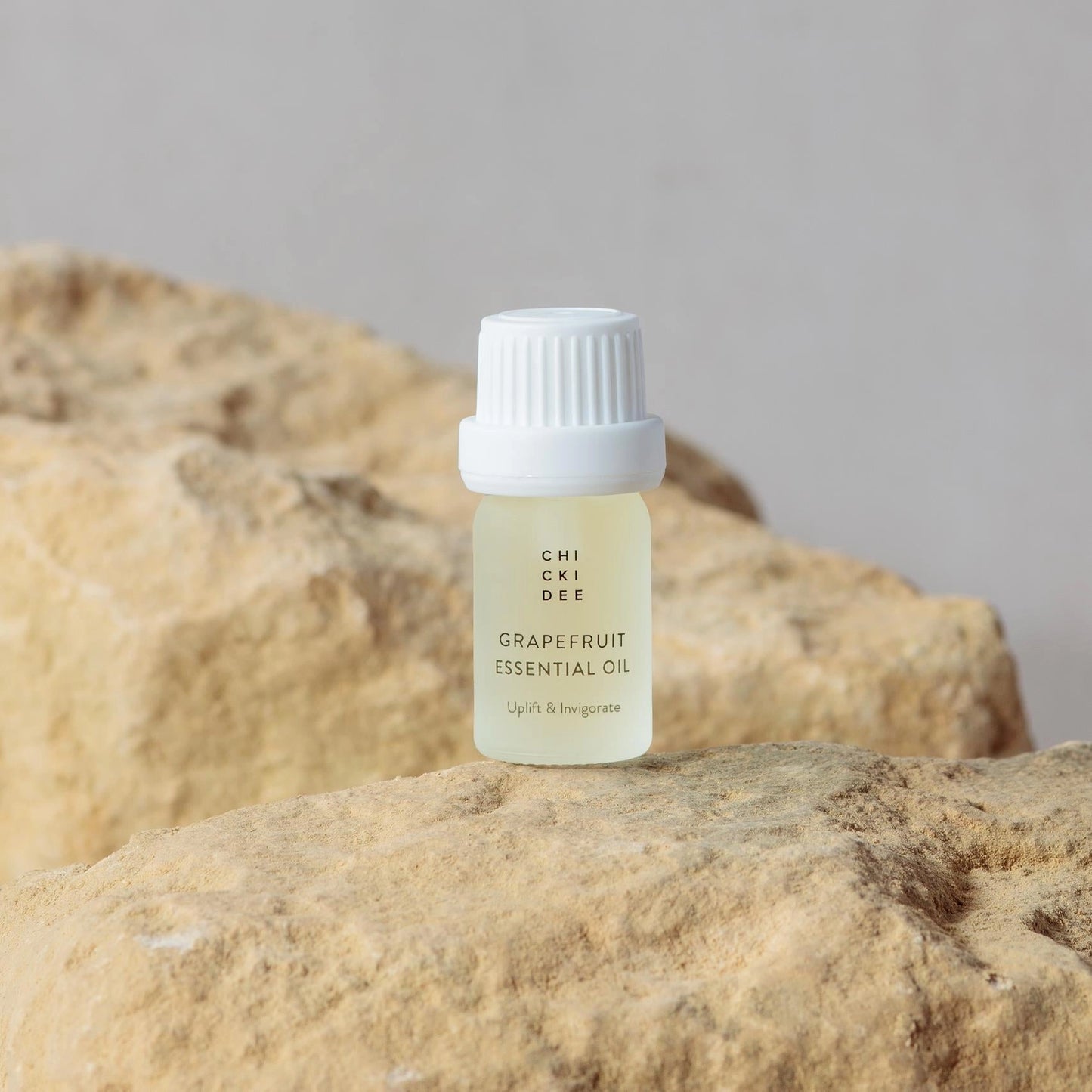 5ml small glass jar with cap filled with grapefruit essential oil on a rock