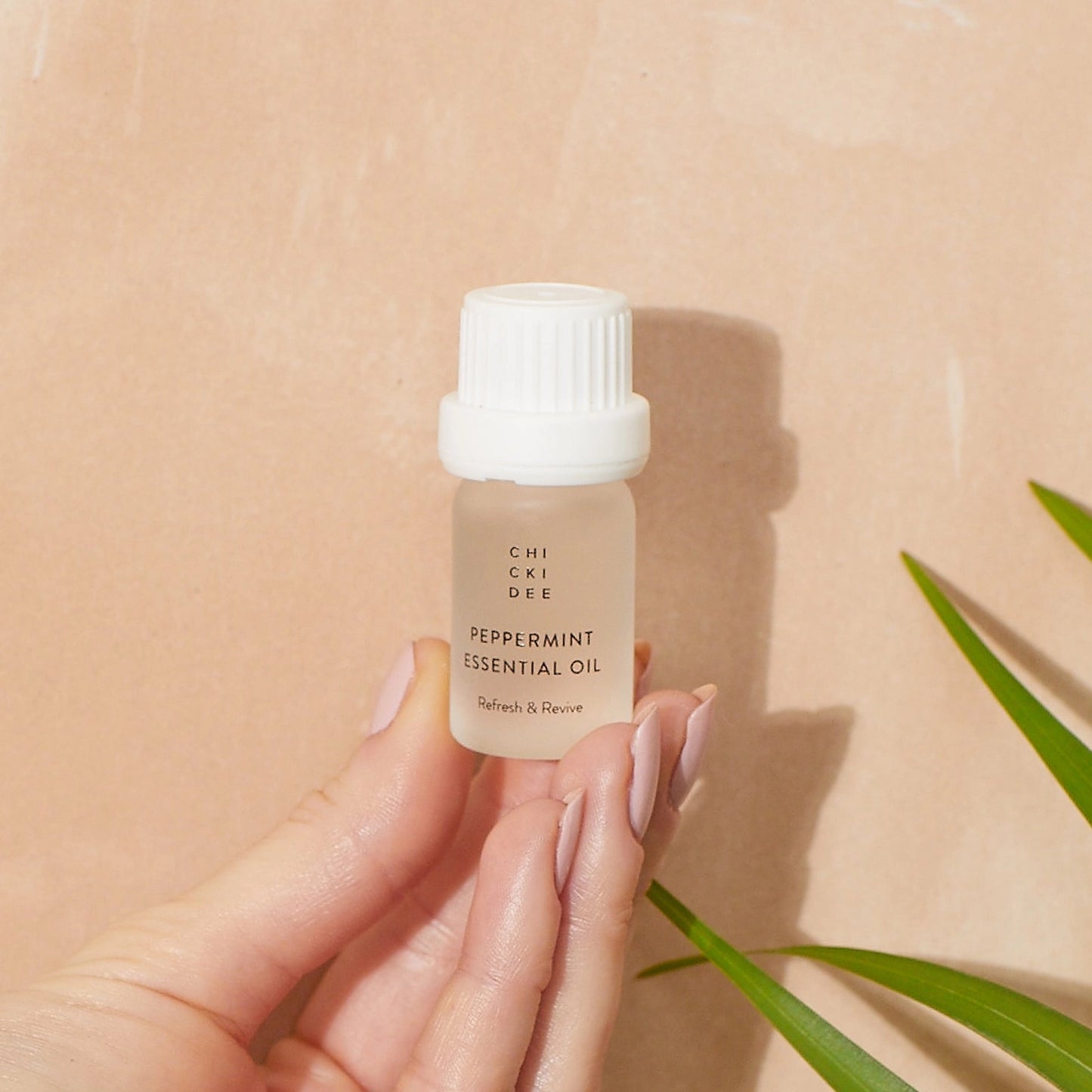 hand with blush colored nail polish holding a small glass bottle with essential peppermint oil