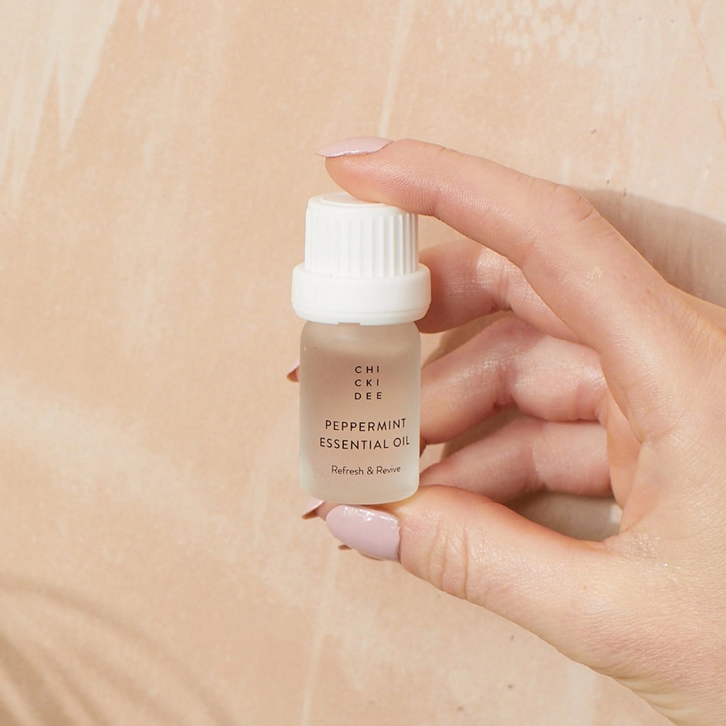hand with blush colored nailpolish holding a small glass bottle with essential peppermint oil