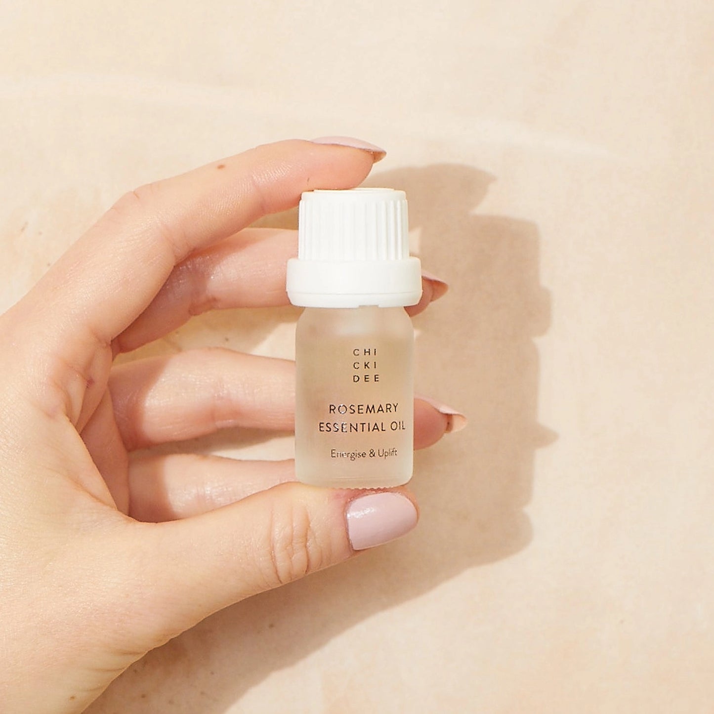 hand holding a small glass bottle with essential rosemary oil