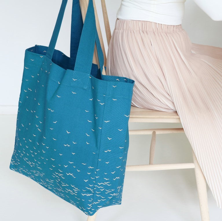 blue cotton tote with birds on hanging on a chair with woman with pink skirt