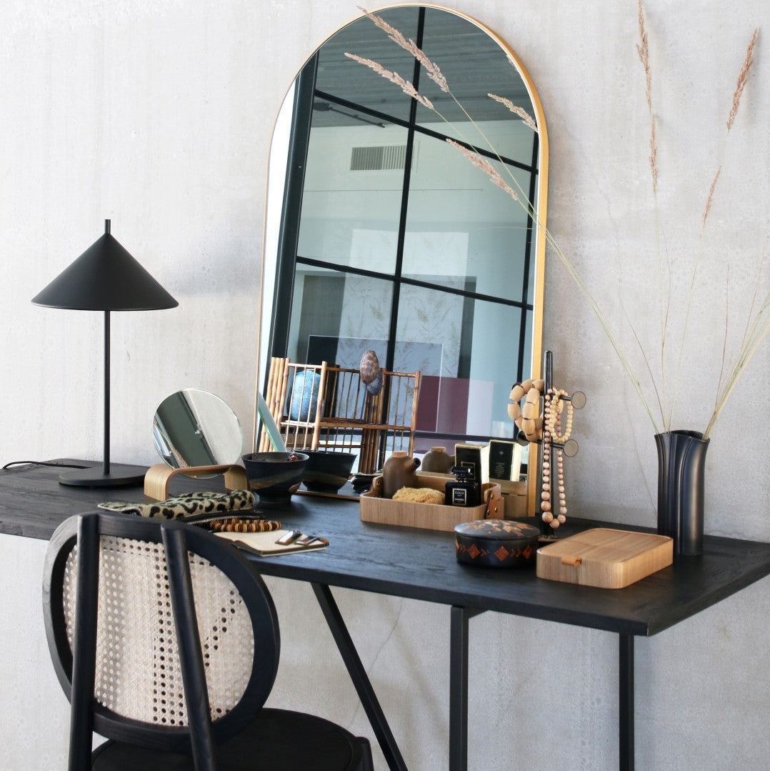 black vanity with cane webbing chair and arch shaped brass mirror