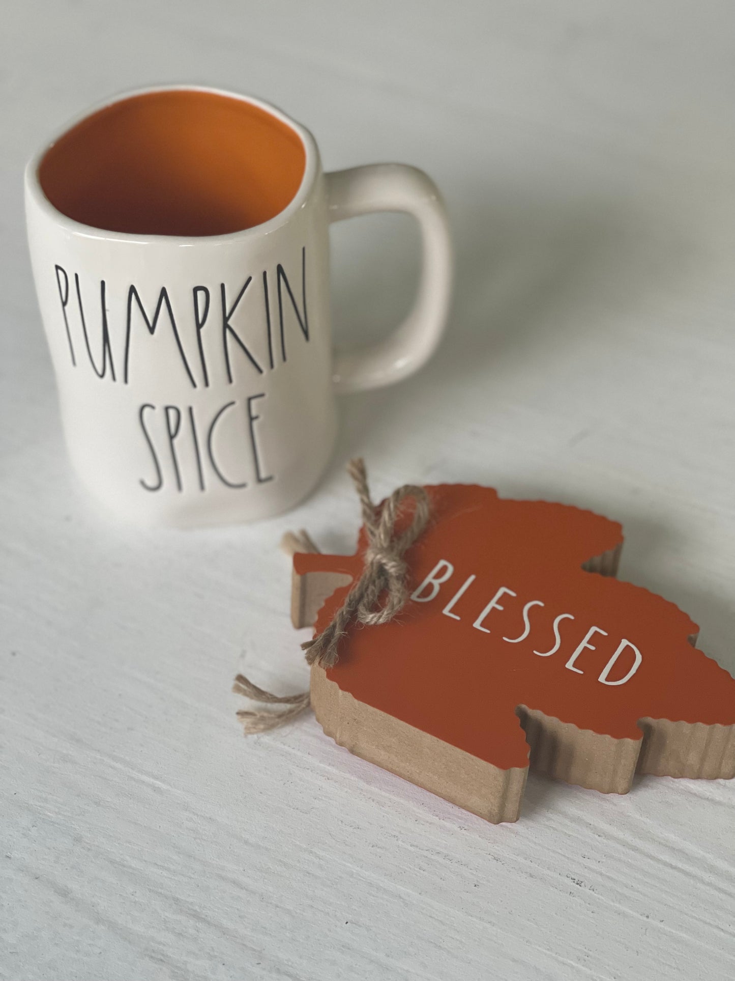 Rae Dunn  mug with pumkin Spice engraving and orange inside on a white wooden table with wooden leaf 