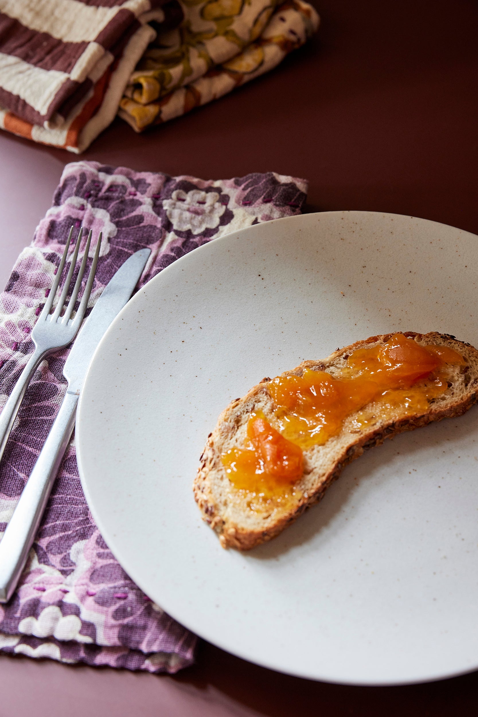 large, white speckled dinner plate with slice of bread and purple flowered napkin