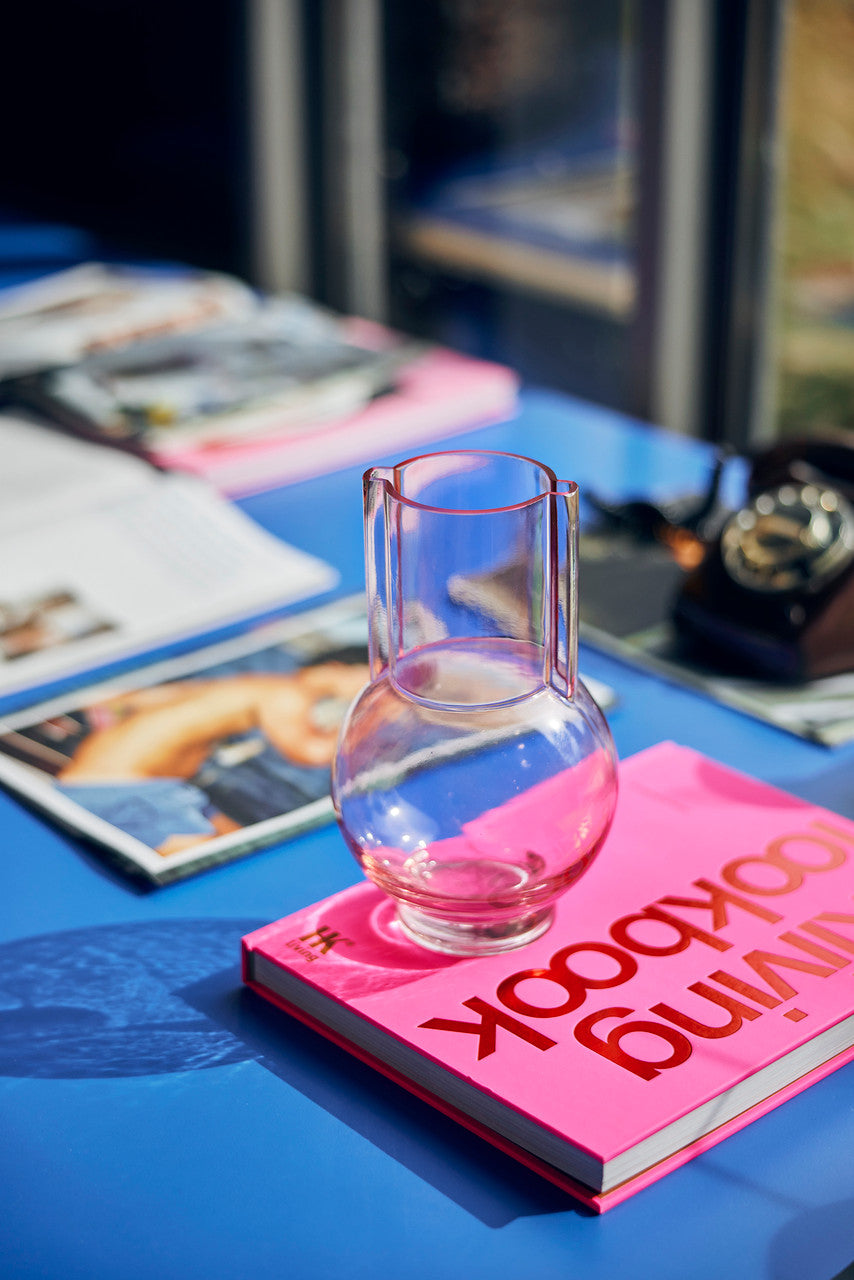 hardcover bright pink look book on a blue table with glass pink vase