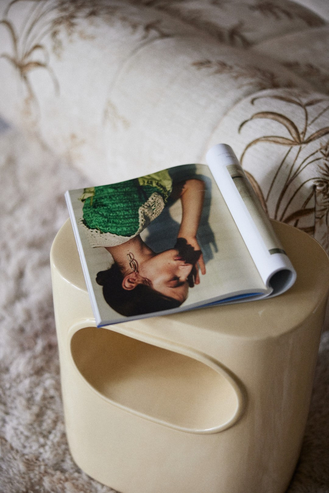 cream colored earthenware accent table with magazine on top