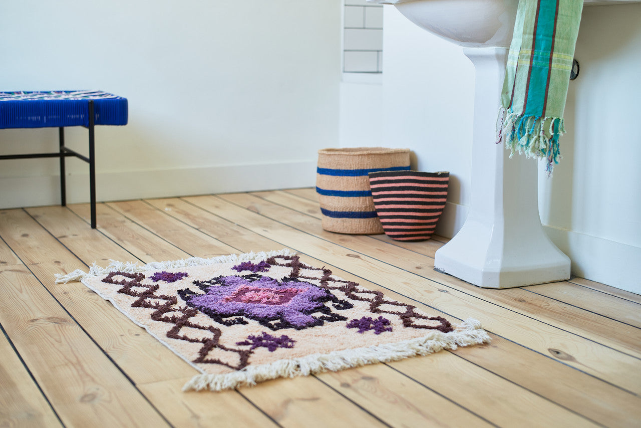salmon colored bath mat rug with brown and purple design on a wooden floor in a bathroom