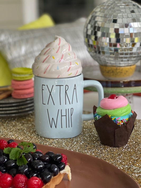powder blue stoneware mug with whipped cream lid on a table with cupcake and fruit cake