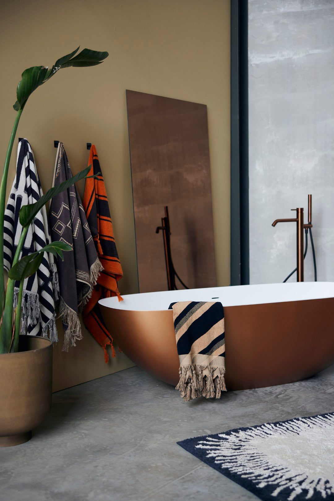 brown and black diagonal striped bath towel with fringes hanging over a brass colored bath tub