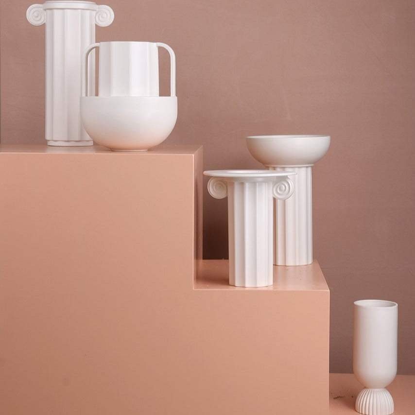 white ceramic vase in a greek column design on a peach colored stairway
