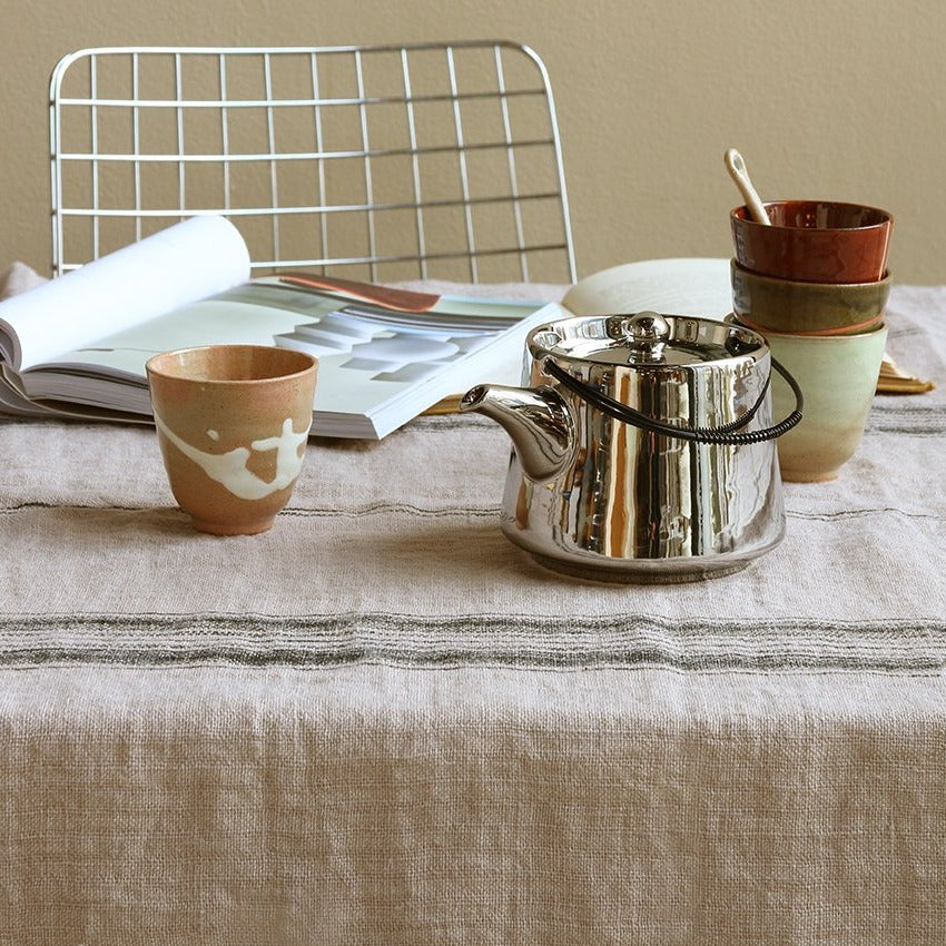 100% natural linen tablecloth in grey with a charcoal accent stripe on a table with silver colored teapot and stoneware mug in brown