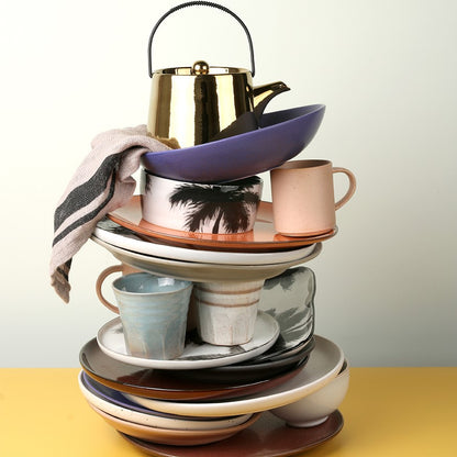 stack of stoneware tableware on a yellow counter with a grey linen napkin on top