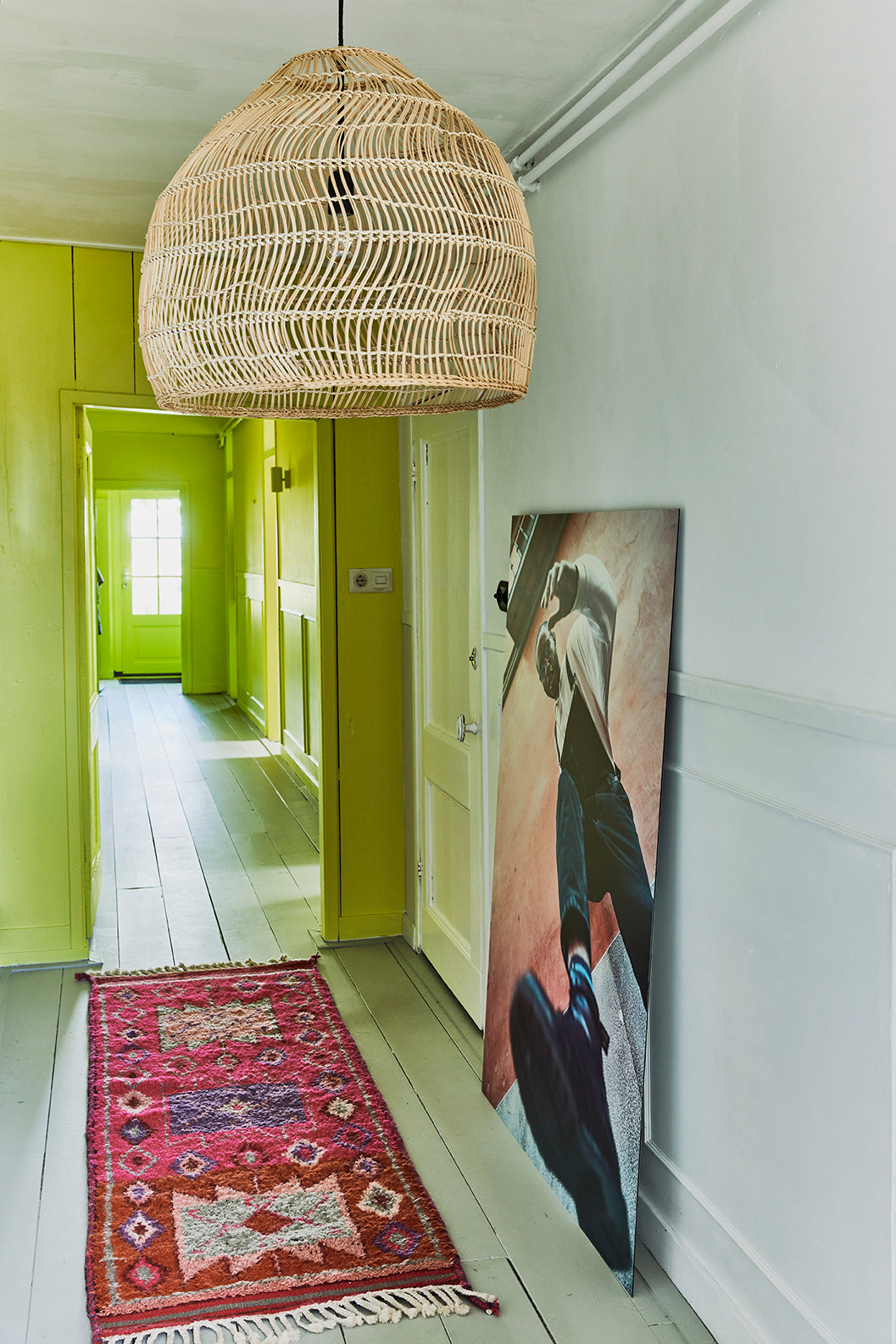 hallway with bright yellow walls, a natural wicker pendant light fixture and a bright pink woolen runner with purple red and gray patterns
