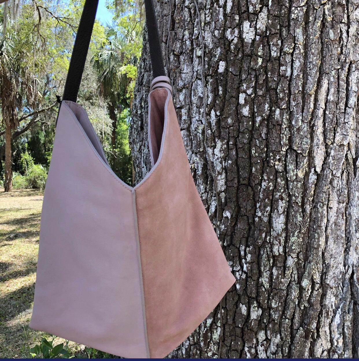 two toned pink leather bag with brown leather shoulder strap hanging on a large oak tree