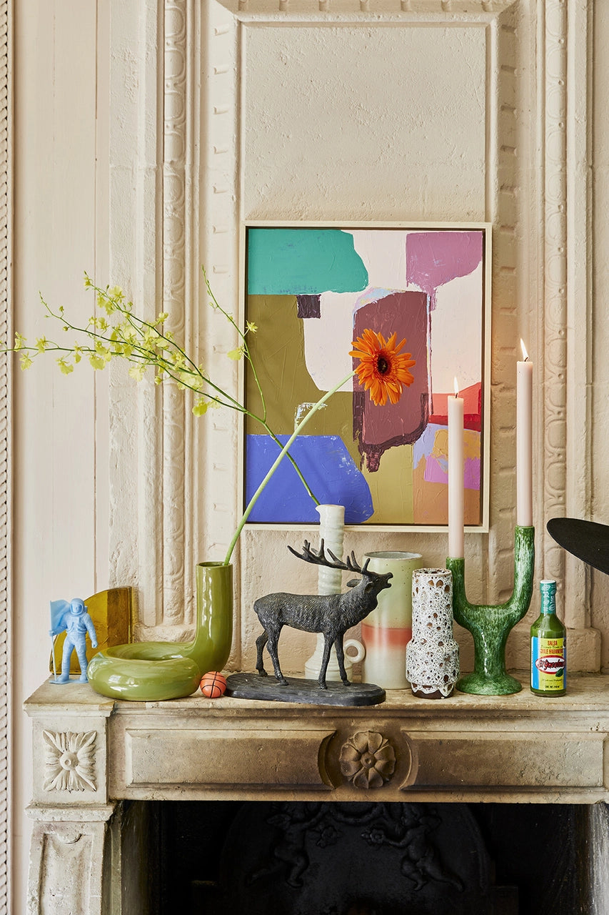 glossy green twisted vase object with a colorfull abstract painting on a fire place mantel