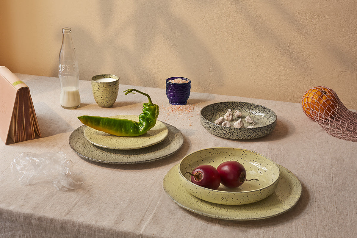 organic shape yellow dinner plates with speckled finish on a table with food and other plates