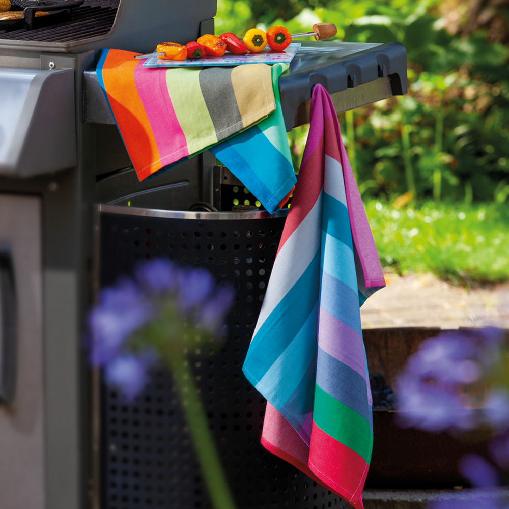 two striped, colorful kitchen towels with big and small stripes hanging on the side of a bbq