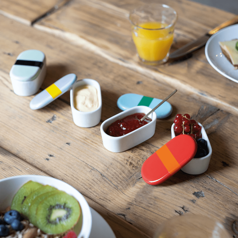 4 porcelain oval boxes with blue lilac green and red  lids with black stripe on table filled with spreads