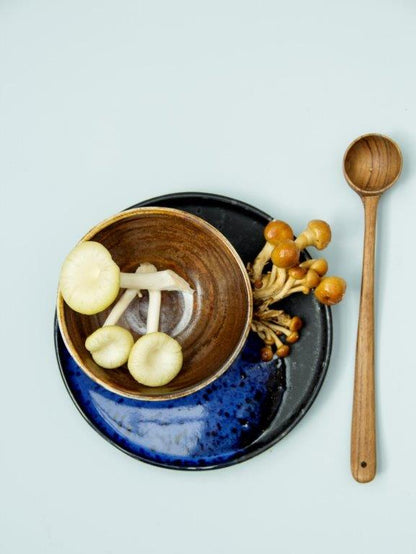 cobalt blue and black dessert plate with mushrooms, a brown bowl and a wooden spoon