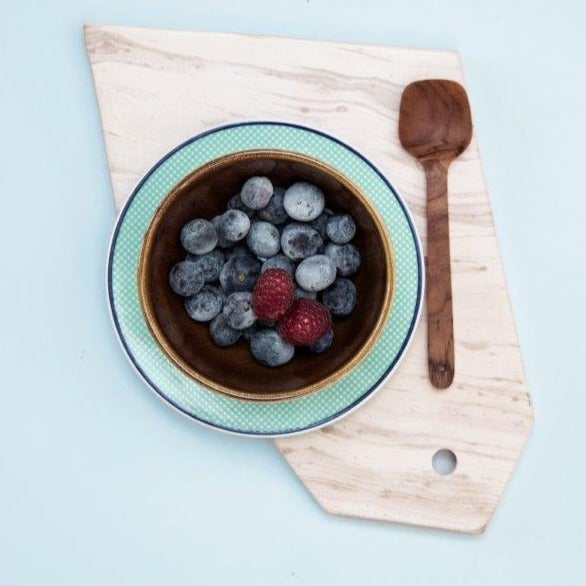 wooden spoon on marble plate with bowl of blueberries