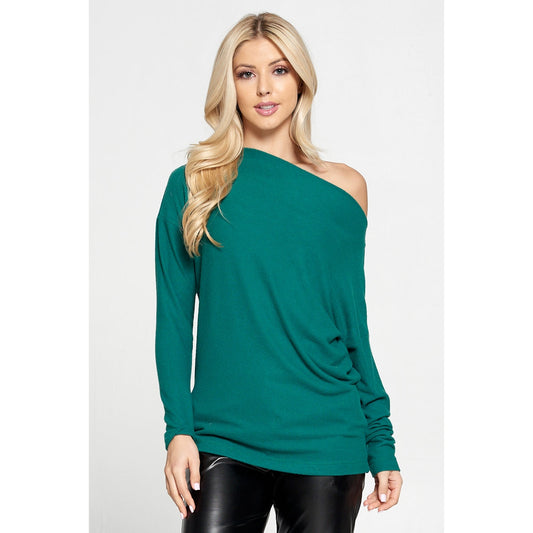 Blonde woman with long hair, black pants and a green off the shoulder knit top 